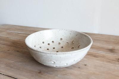 Speckled ceramic colander on a wooden surface with a white background by KJ Pottery