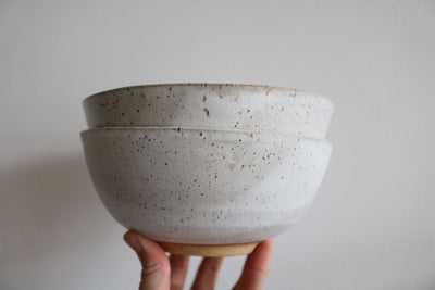 Speckled white handmade ceramic cereal bowls stacked and held in hand