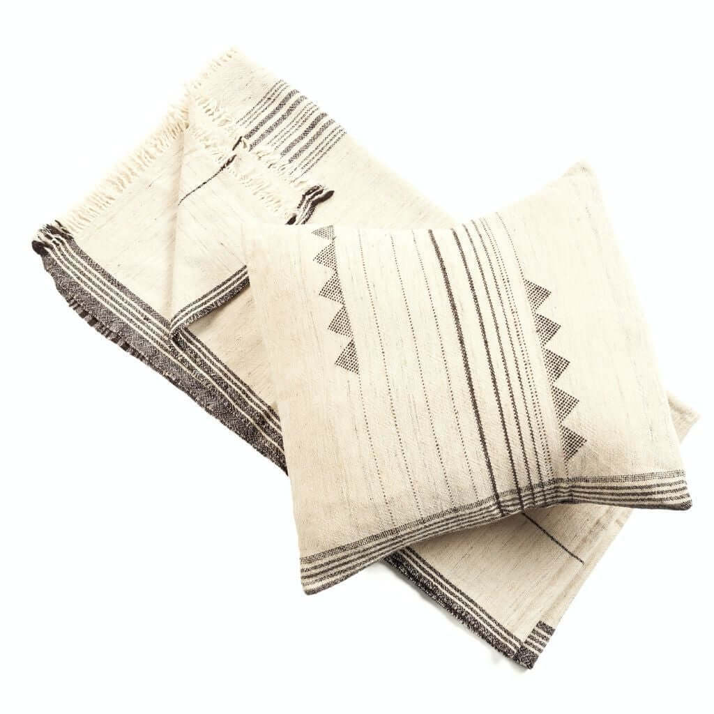 Two folded ivory handloom pillow covers showing black stripes and triangular patterns.