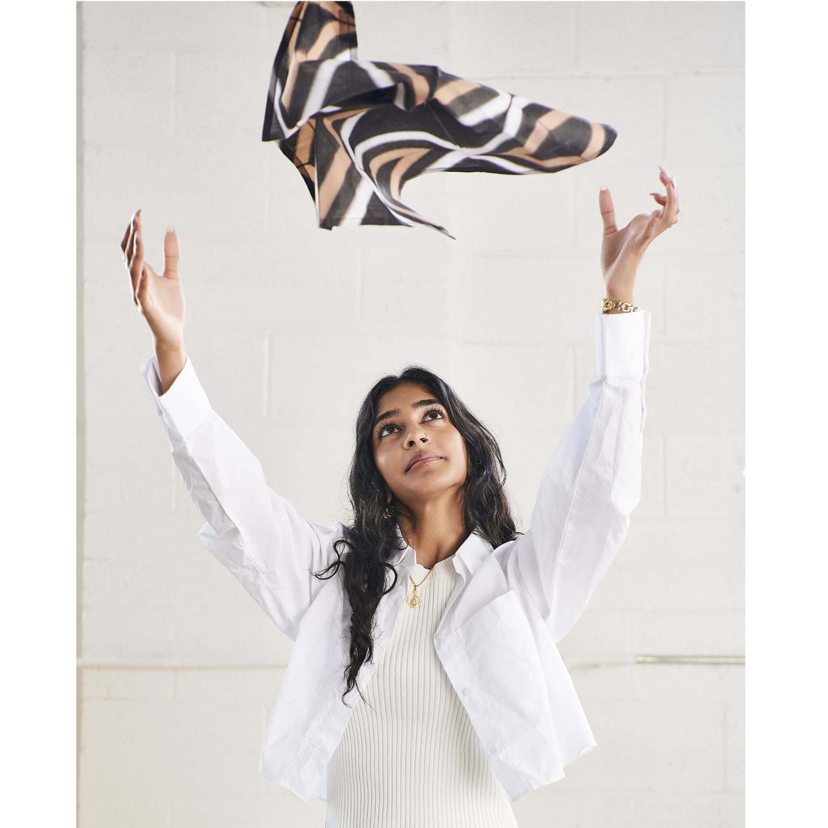 Woman tossing an unfolded patterned napkin into the air to demonstrate its light cotton fabric.