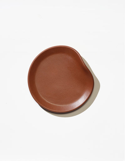Tortuga Forma Bread Plate Single in Tierra viewed overhead on white, showing its glazed finish, subtly textured centre and gently asymmetrical raised rim.