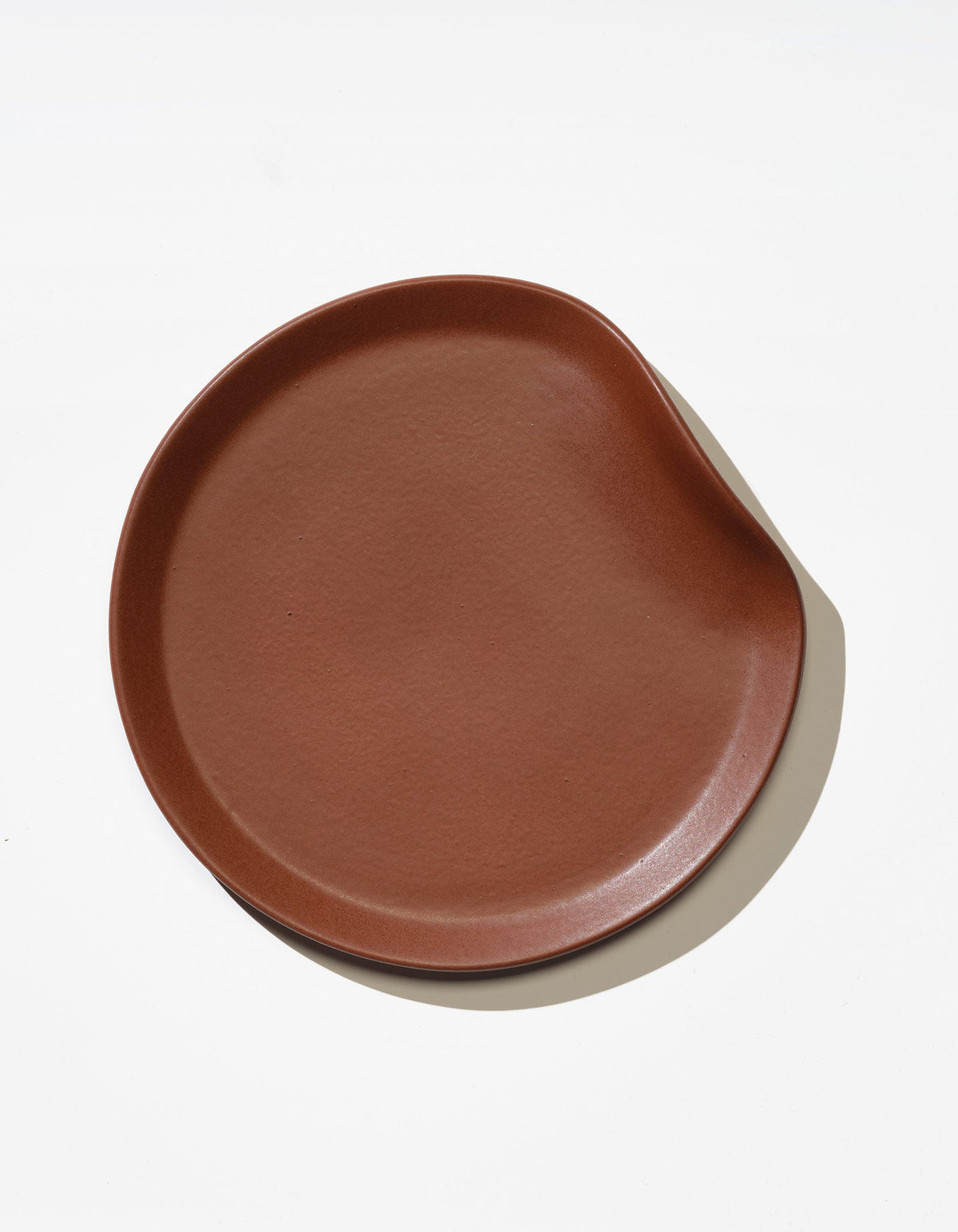 Tortuga Forma Salad Plate Single in Tierra viewed overhead on white, showing its glazed surface, fine texture and softly rounded rim with an indentation on one side.