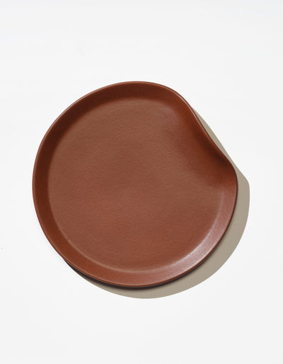 Tortuga Forma Salad Plate Single in Tierra viewed overhead on white, showing its glazed surface, fine texture and softly rounded rim with an indentation on one side.