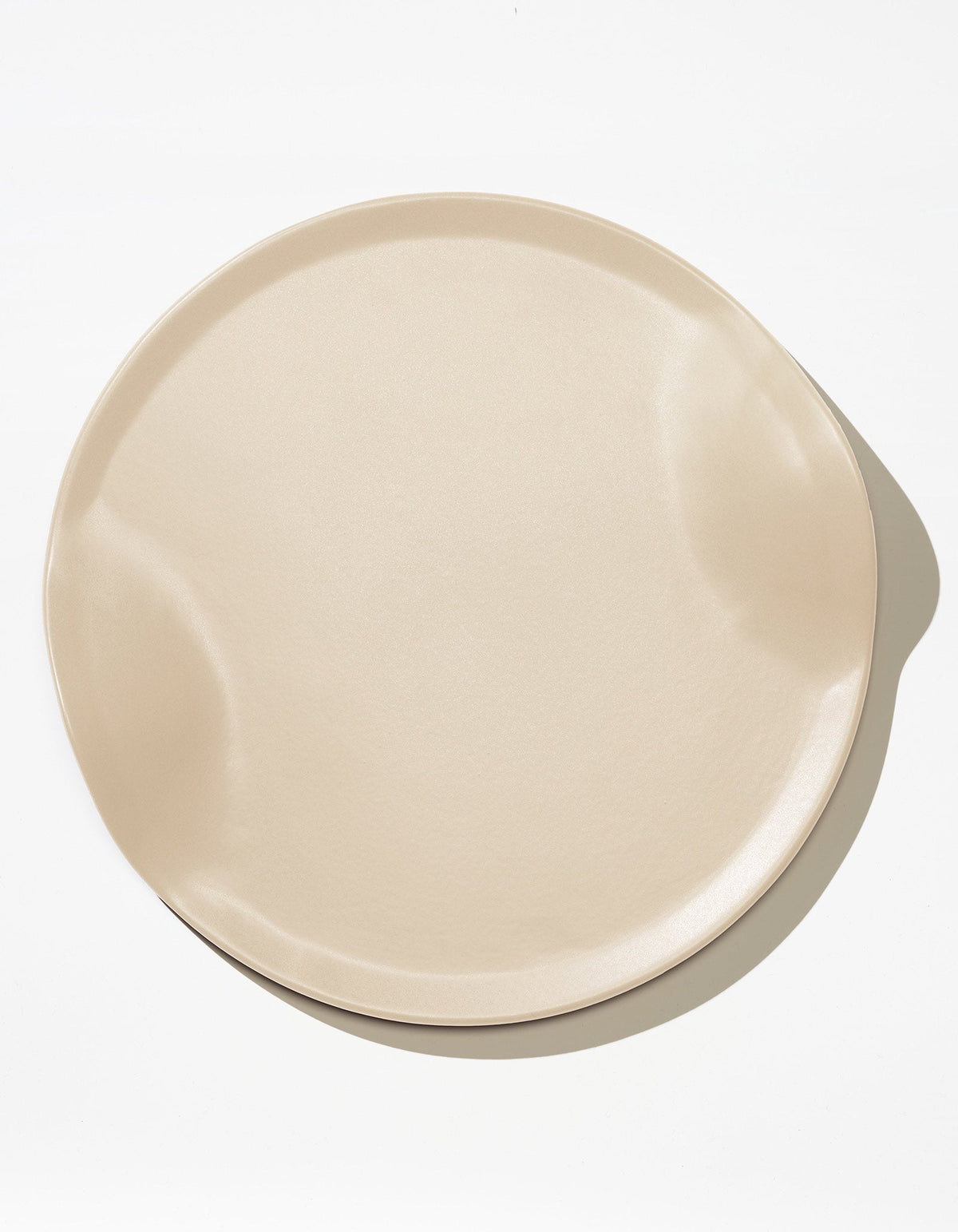 Tortuga Forma Serve Platter in Bone off-white viewed overhead on white, showing a broad round centre, shallow raised rim and two opposing inward curves, with light reflecting across its smooth glazed surface.
