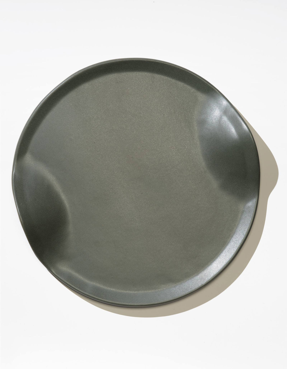 Tortuga Forma Serve Platter in Liche dark grey viewed overhead on white, showing its shallow round form, raised edge and opposing curved indentations, with a glossy highlight along one side.
