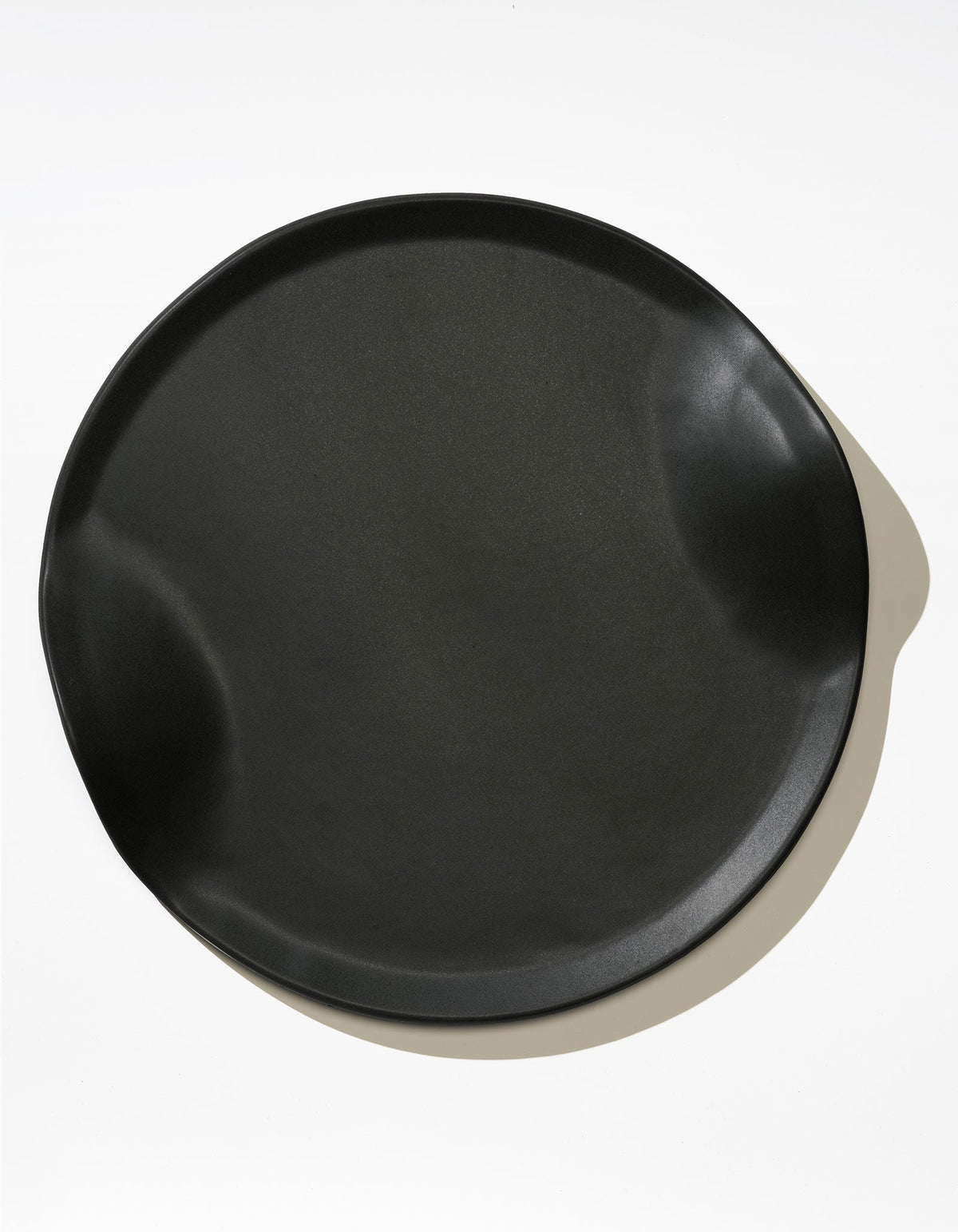 Tortuga Forma Serve Platter in Soot black viewed overhead on white, showing a broad serving surface, low raised rim and two opposing inward curves, with reflected light highlighting the smooth finish.