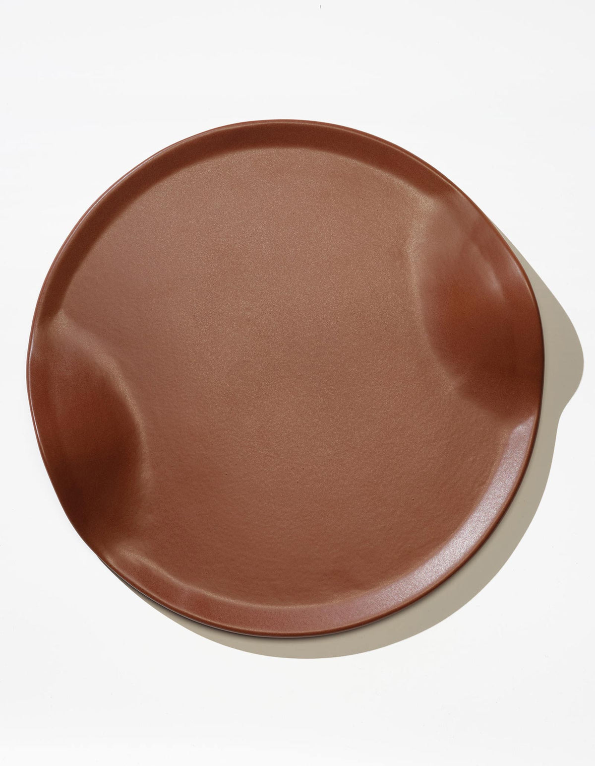 Tortuga Forma Serve Platter in Tierra terra cotta viewed overhead on white, showing its reddish-brown glazed surface, shallow raised rim and opposing curved indentations.