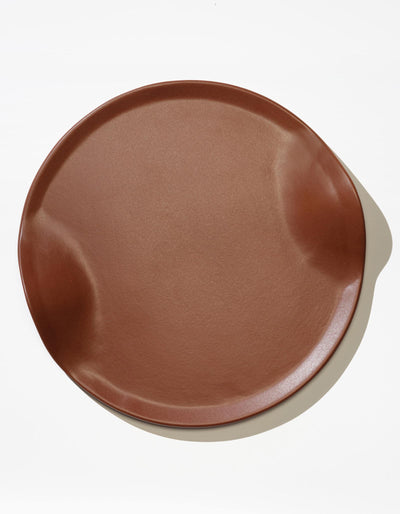 Tortuga Forma Serve Platter in Tierra terra cotta viewed overhead on white, showing its reddish-brown glazed surface, shallow raised rim and opposing curved indentations.