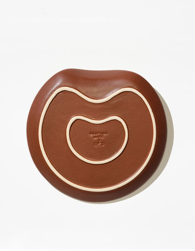 Underside of Tortuga Forma Salad Plate Single in Tierra, showing two cream-coloured raised outlines following its irregular shape and a central maker’s mark that is too small to read.