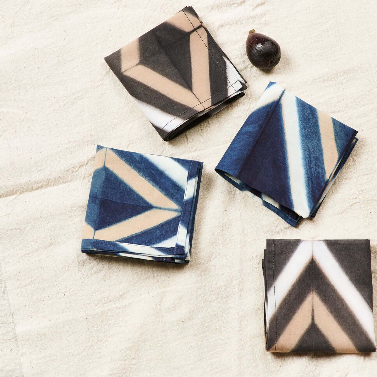 Black and blue Tisa napkins folded into different shapes on a light tablecloth.