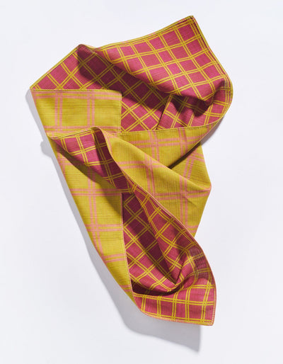 Loosely draped Tortuga Forma Dinner Napkins Double Sided Grid - High Season revealing contrasting burgundy-and-yellow and mustard-and-pink grid patterns, with stitched edges and soft folds visible.