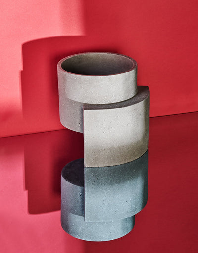 Graphite Tortuga Forma Platform Planter Medium Terrazzo on a mirrored surface against a vivid red backdrop, with its geometric form reflected below and a strong shadow cast behind.