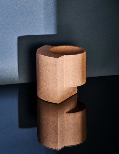 Coral Tortuga Forma Platform Planter Small - Terrazzo on a glossy black surface, casting a clear reflection against a blue-grey backdrop, with light highlighting its circular opening and geometric slab support.
