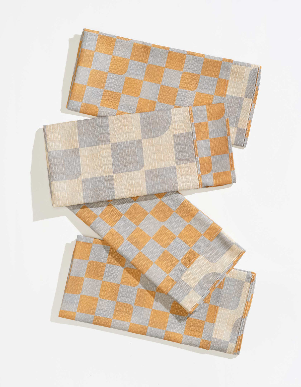 Four Tortuga Forma Dinner Napkins Double Sided Checker - Quiet Season folded and overlapped on white, showing mustard-yellow and pale grey checks alongside a cream-and-grey reverse, with fine woven texture and stitched hems.