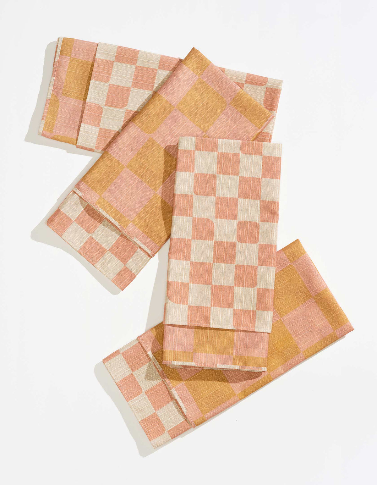 Four folded Tortuga Forma Dinner Napkins Double Sided Checker - Quiet Season arranged on white, showing coral-and-cream checks and a contrasting pink-and-mustard reverse with neatly stitched borders.