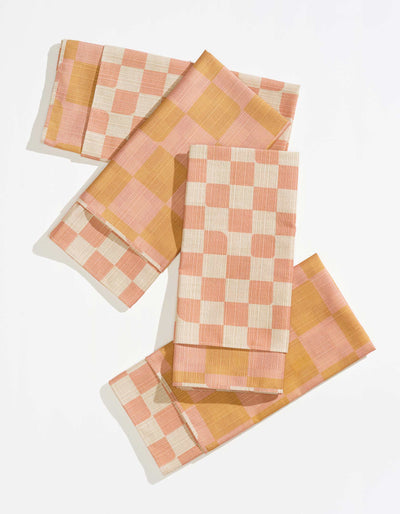 Four folded Tortuga Forma Dinner Napkins Double Sided Checker - Quiet Season arranged on white, showing coral-and-cream checks and a contrasting pink-and-mustard reverse with neatly stitched borders.