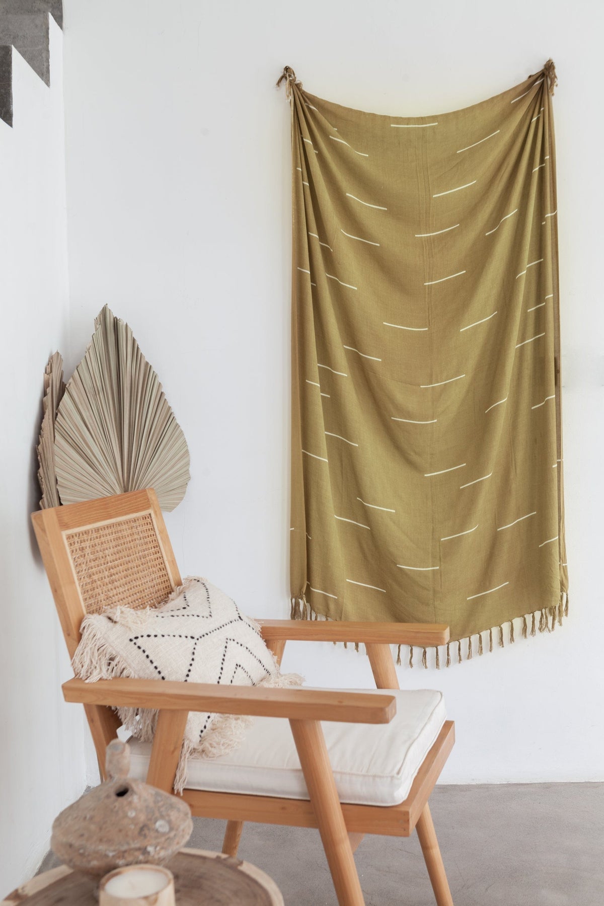 Village Thrive Lines Tapestry, olive gold rayon, hanging above a wooden chair with a woven basket.