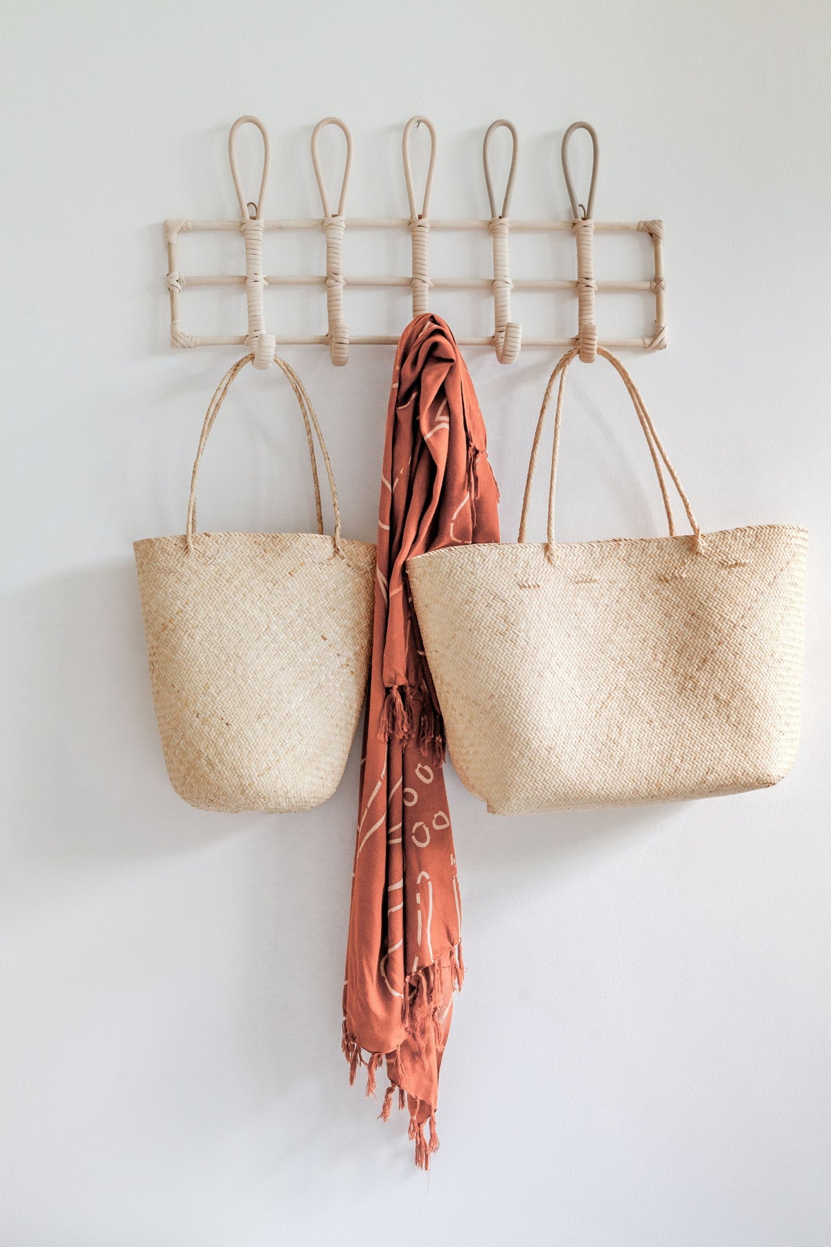 Village Thrive Praya Day Bag, natural rattan with black wave pattern, two bags hanging on wall hooks with a printed scarf.
