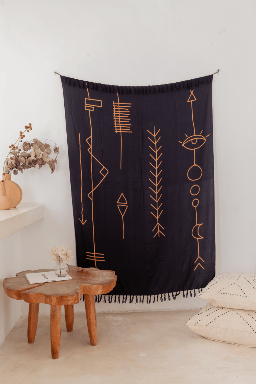Village Thrive Abstract Tapestry, navy rayon, hanging above a round wood table with a floor cushion.