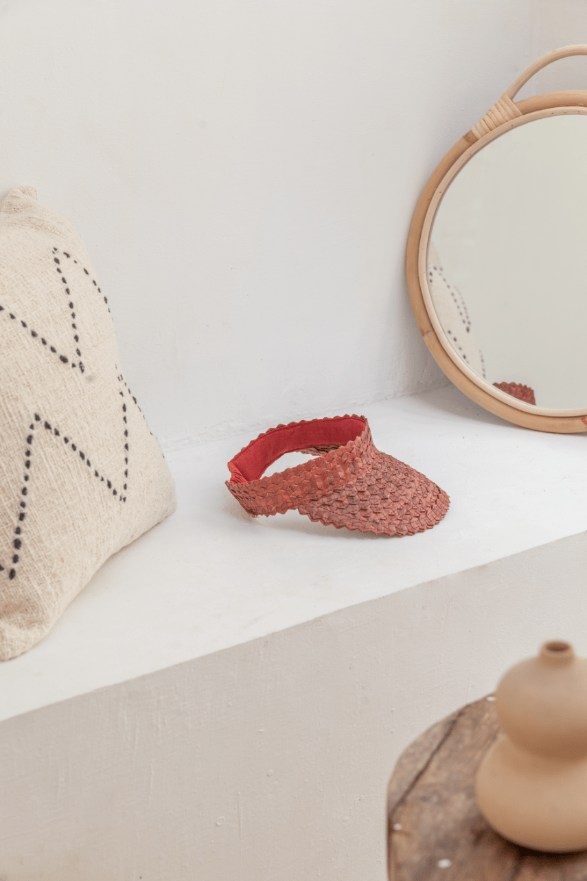 Village Thrive Rattan Sun Visor, amber palm leaf, displayed on a shelf beside a round mirror.