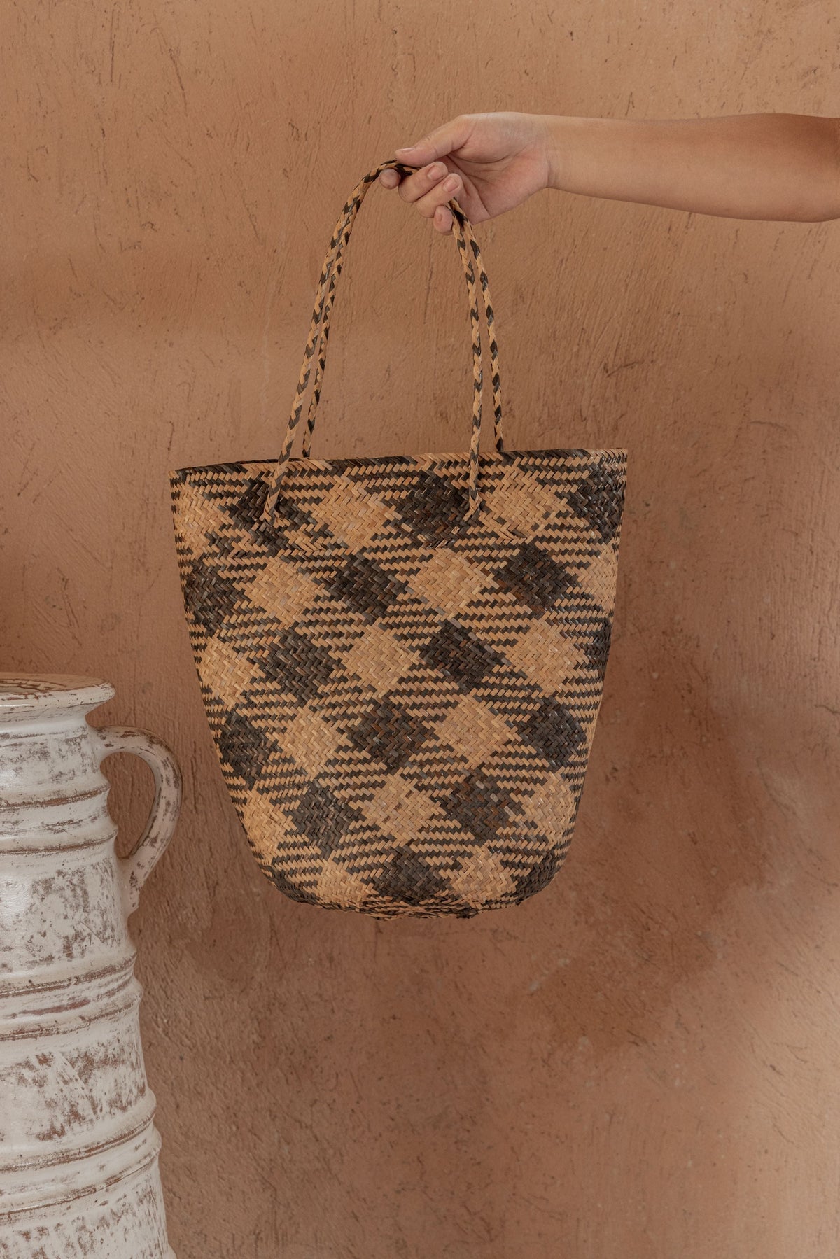 Village Thrive Praya Day Bag, black and tan plaid rattan, close-up of hand holding the handle.
