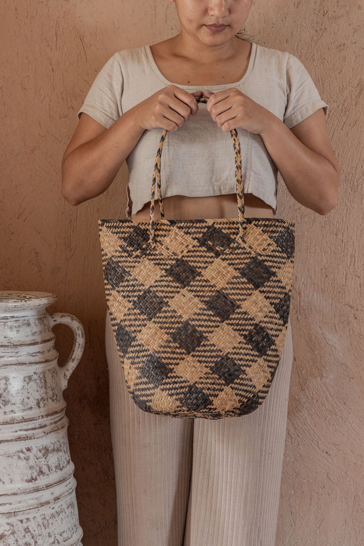 Village Thrive Praya Day Bag, black and tan plaid rattan, worn by a model holding the handles.