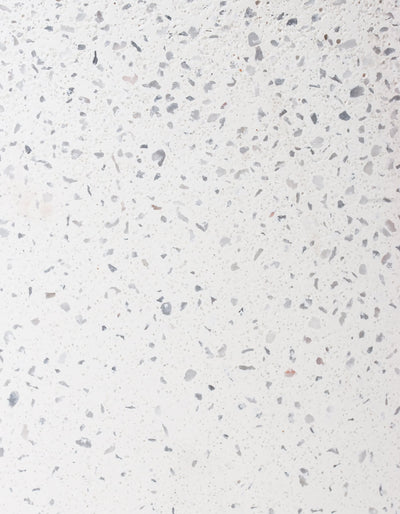 Close-up of the white finish on the Tortuga Forma Platform Planter Small - Terrazzo, showing irregular grey and pale beige chips scattered across an off-white background.