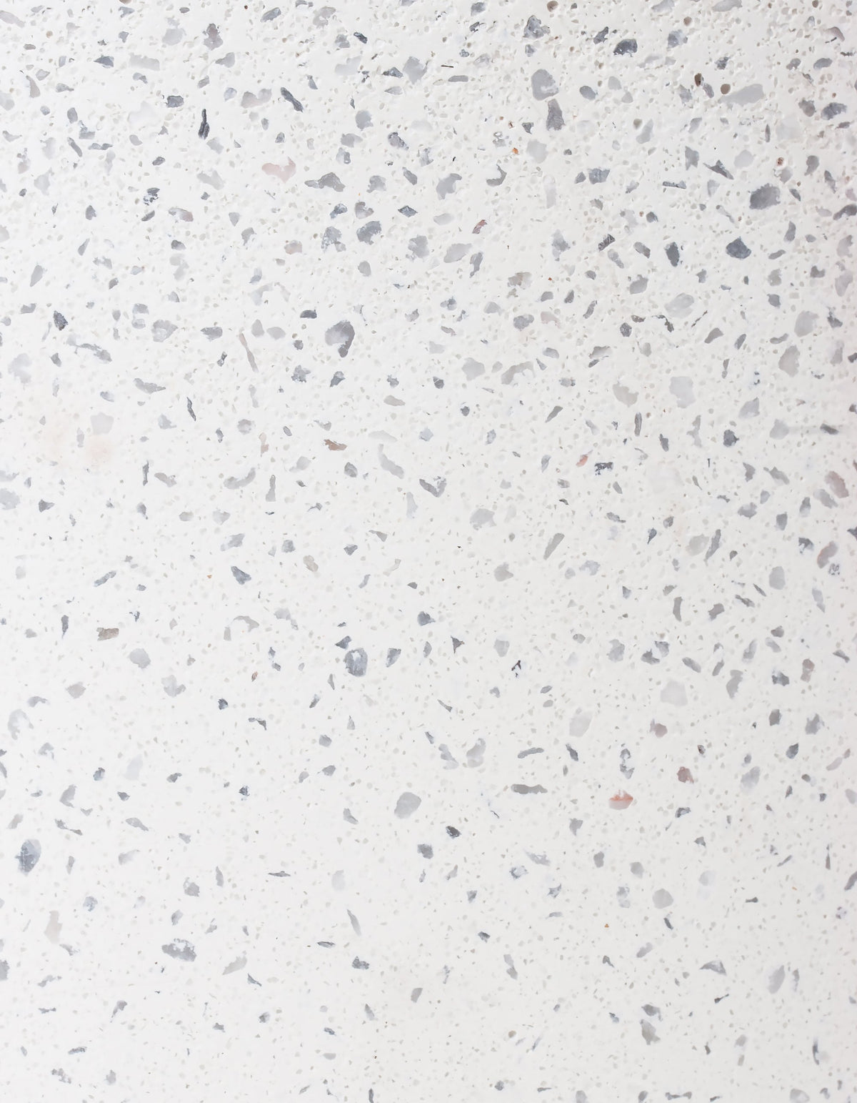 Close-up of the white Tortuga Forma Platform Planter Medium Terrazzo finish, showing irregular grey and pale beige chips scattered across an off-white background.