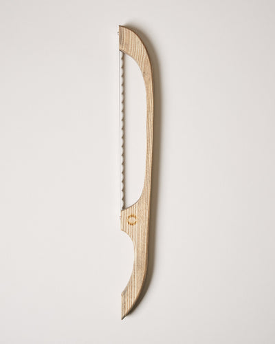 Natural light-wood bread bow with an elongated curved frame and serrated blade shown against a neutral backdrop.