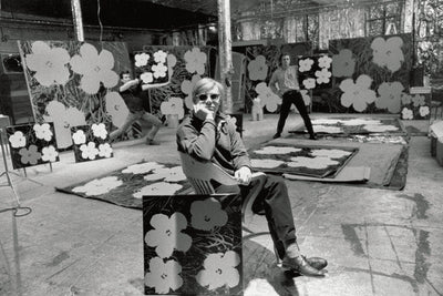 Black-and-white archival photograph of an artist seated among large floral artworks.