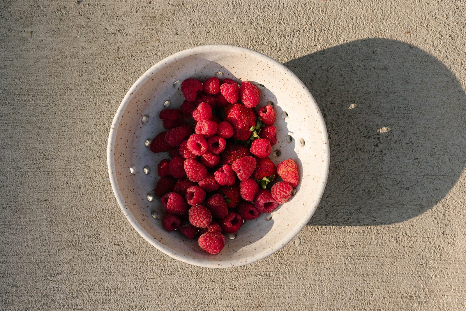 White ceramic colander filled with raspberries on a concrete surface, by KJ Pottery