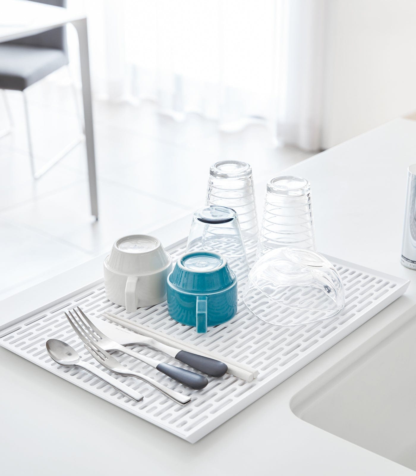 White drying mat with cutlery, glasses, and bowls on a kitchen counter.