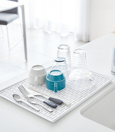 White drying mat with cutlery, glasses, and bowls on a kitchen counter.