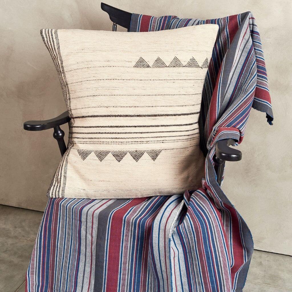 Ivory geometric pillow displayed on a chair draped in colorful striped fabric.