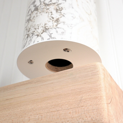 Low-angle detail of the pale wood base’s underside, showing a circular opening and metal fasteners.