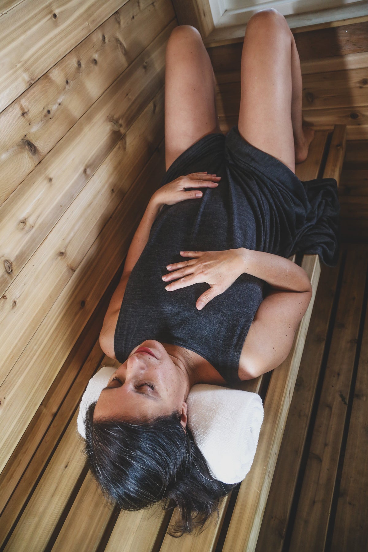 Woman resting in a merino wool sauna dress during a sauna and recovery ritual, highlighting comfort and natural movement.