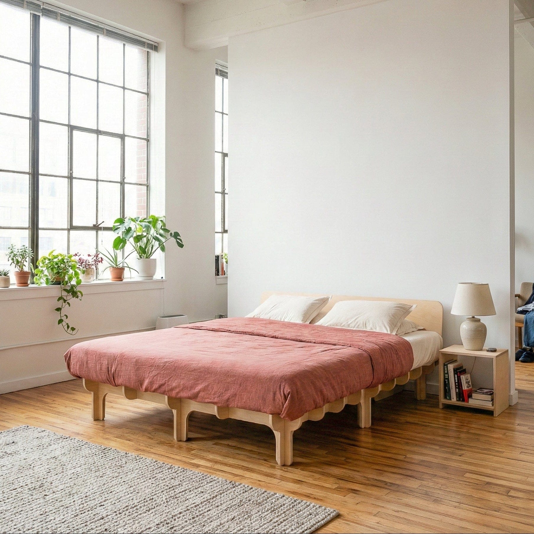Studio Furnis DOVID natural wood bed frame with dusty rose bedding, a low curved headboard and multiple rounded legs in a bright loft bedroom filled with plants