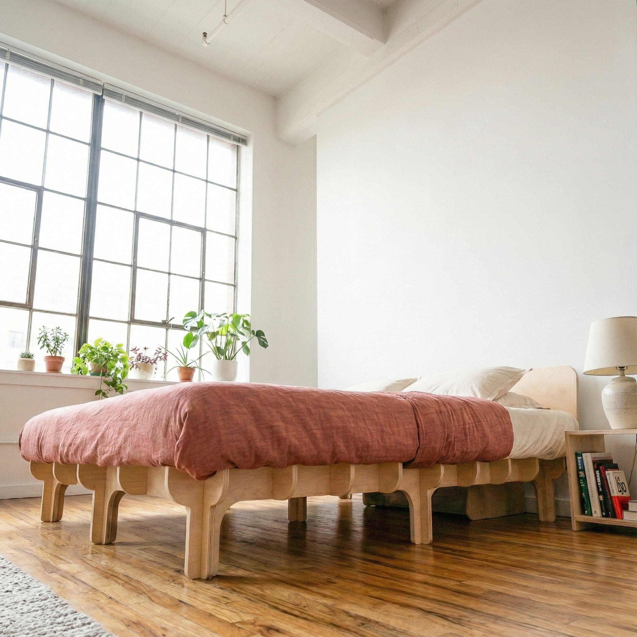 Side view of the DOVID bed frame with dusty rose bedding, showing the natural wood platform, curved headboard and evenly spaced rounded legs