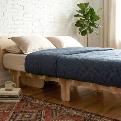 Close-up of the DOVID bed frame with dark blue bedding, highlighting its thick wood platform edge and multiple rounded support legs