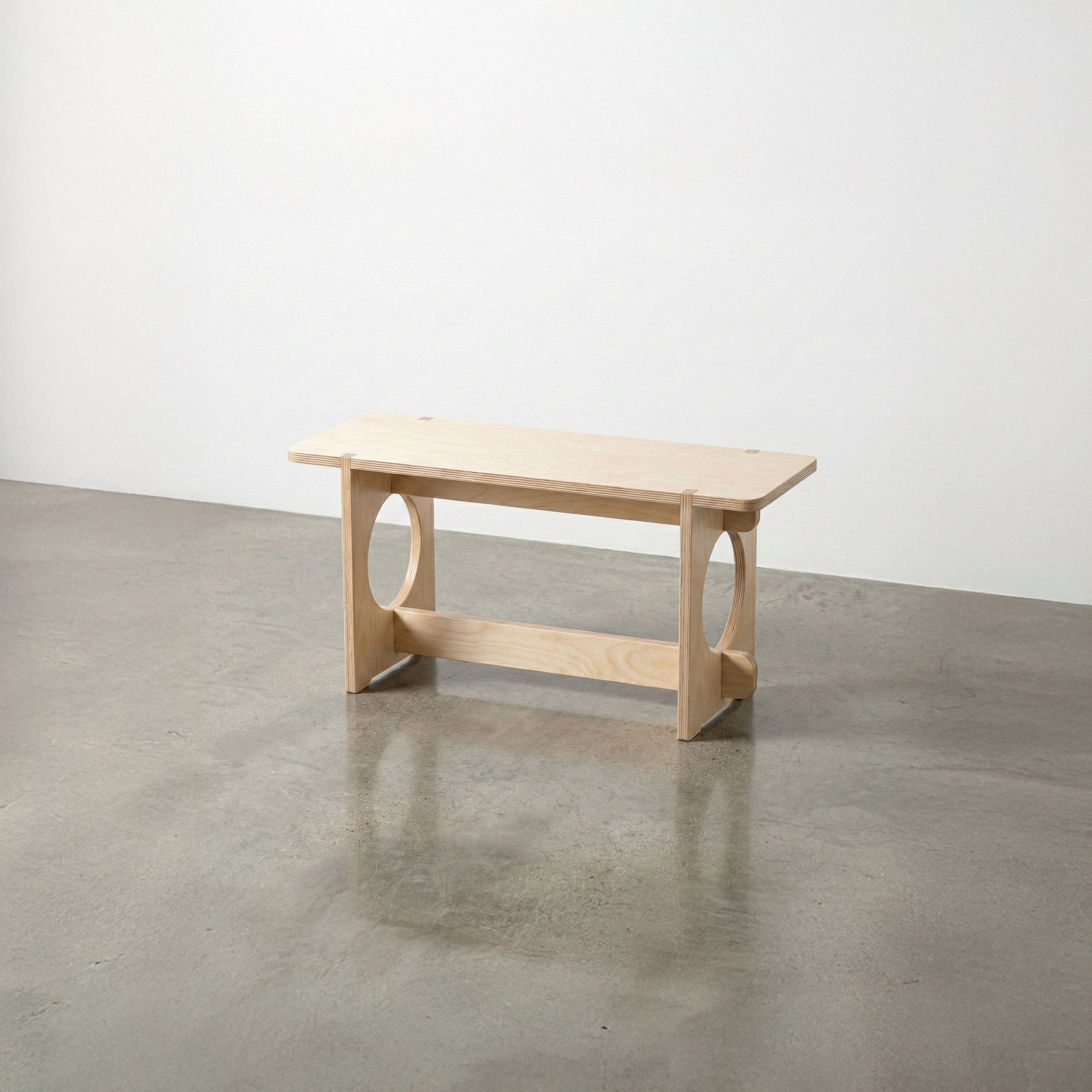 Studio Furnis YOYO natural wood bench with a rectangular seat, rounded corners, circular side openings and a low support rail on a polished concrete floor