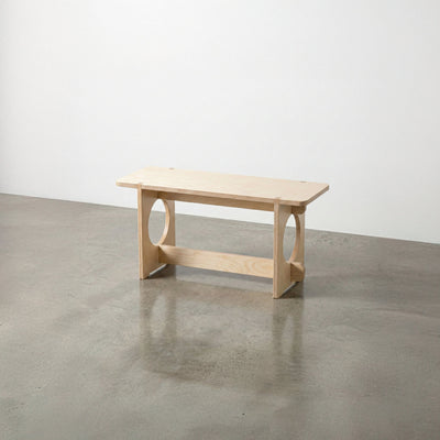 Studio Furnis YOYO natural wood bench with a rectangular seat, rounded corners, circular side openings and a low support rail on a polished concrete floor