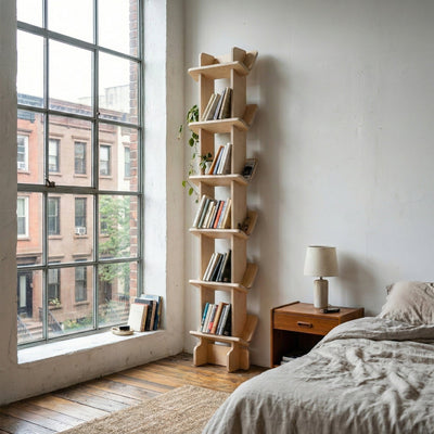 Yankel natural wood bookcase filled with books beside floor-to-ceiling loft windows and a neatly made bed