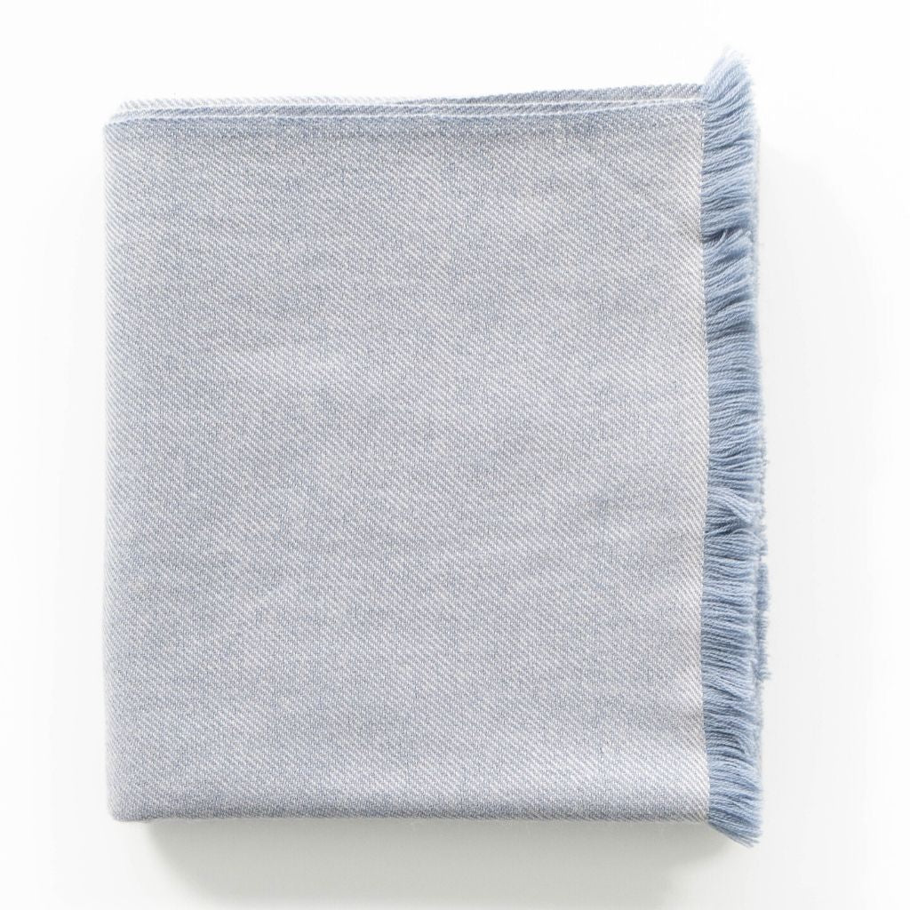 Folded pale blue-gray color variation of the Variously merino throw with soft blue fringe