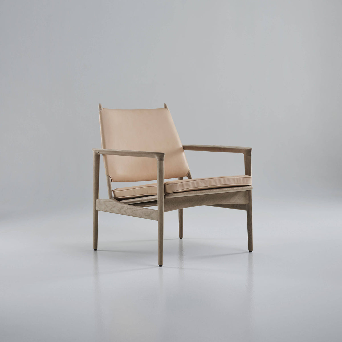 Three-quarter view of the Eikund Broadway Lounge Chair with pale tan leather and a light wood frame in a gray studio, showing its reclined back, slim cushion, and rectangular side frames.