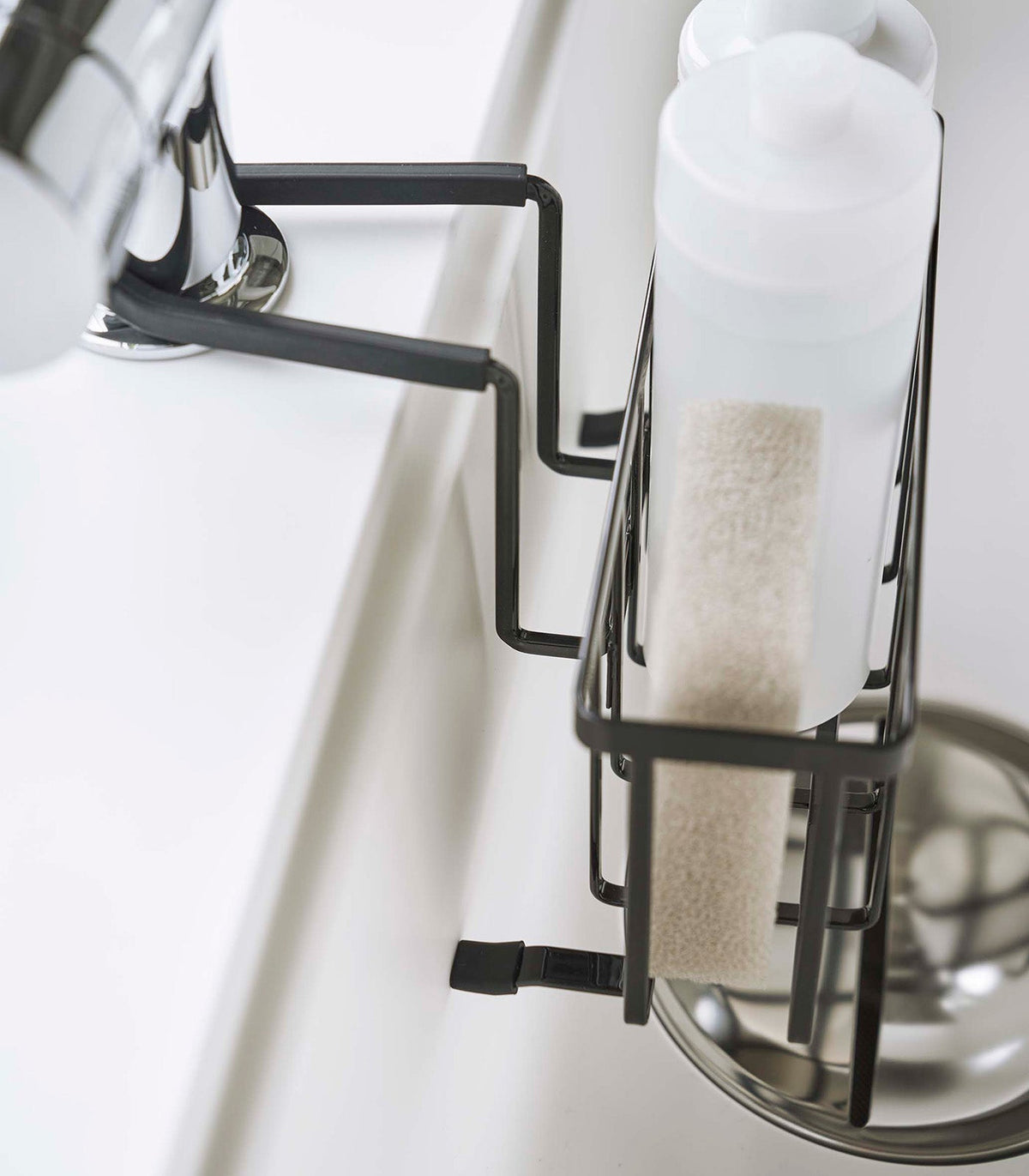 Side detail of the black Yamazaki Home Faucet-Hanging Sponge Caddy - Steel, revealing the narrow wire basket, upright sponge, white bottle and angular support arms.