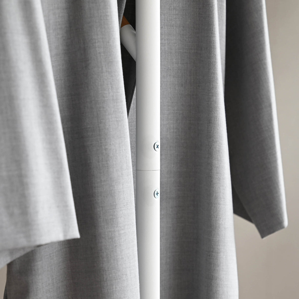 Detail of the white Yamazaki Home Coat Rack (70" H) - Steel pole behind a hanging grey coat, showing a joint and two visible screw heads.