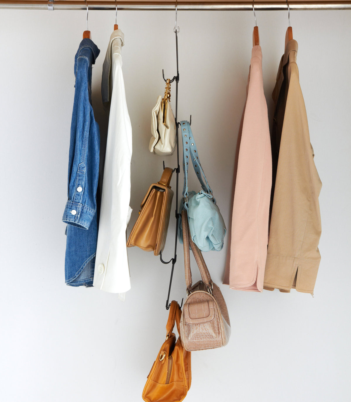 Black Yamazaki Home Cascading Storage Hooks - Steel suspended from a wardrobe rail between hanging clothes, holding small handbags at staggered heights.