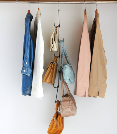 Black Yamazaki Home Cascading Storage Hooks - Steel suspended from a wardrobe rail between hanging clothes, holding small handbags at staggered heights.