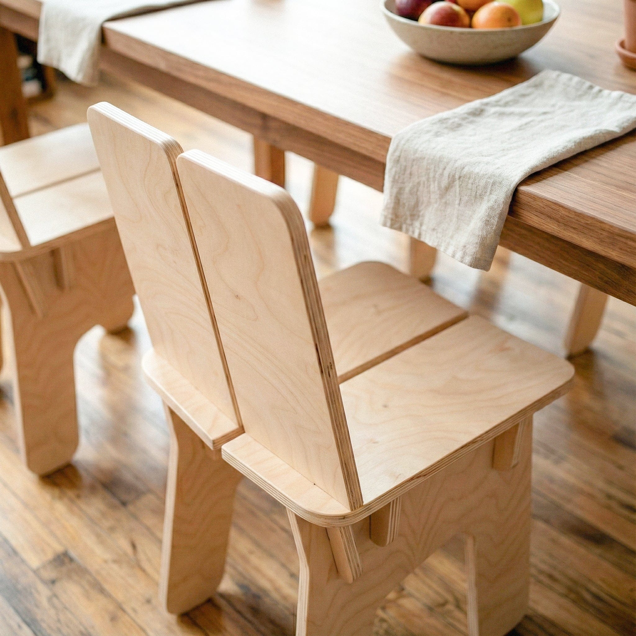 Close rear view of the BURIJ chair at a wood dining table, highlighting its split backrest, visible wood grain and angular construction