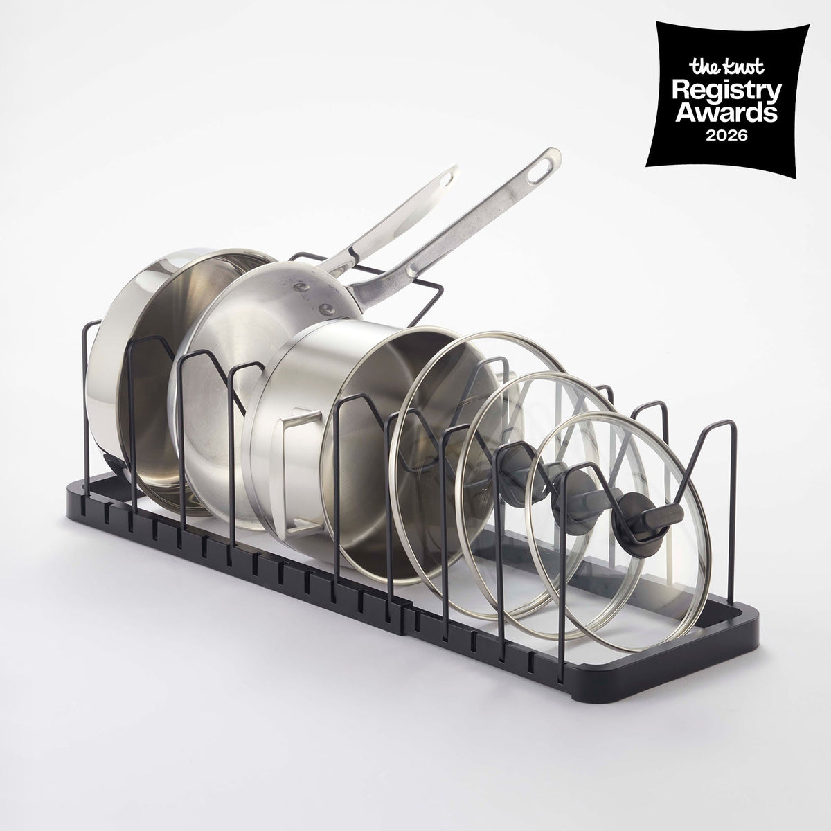 Angled product view of the black Yamazaki Home Adjustable Pot Lid Organizer - Steel, showing upright cookware separated by black wire dividers along its rectangular base.
